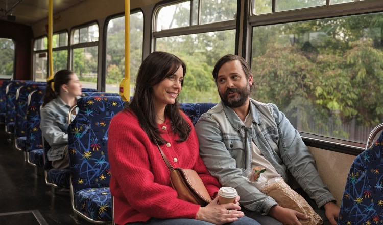 A woman and a man sit in the bus smiling in conversation